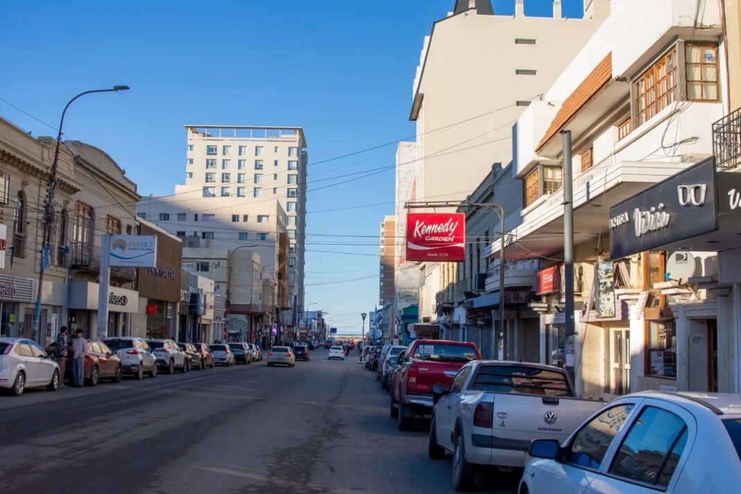 Calle comercial en Comodoro Rivadavia con locales con carteles de 'Se vende' o 'Se alquila'.