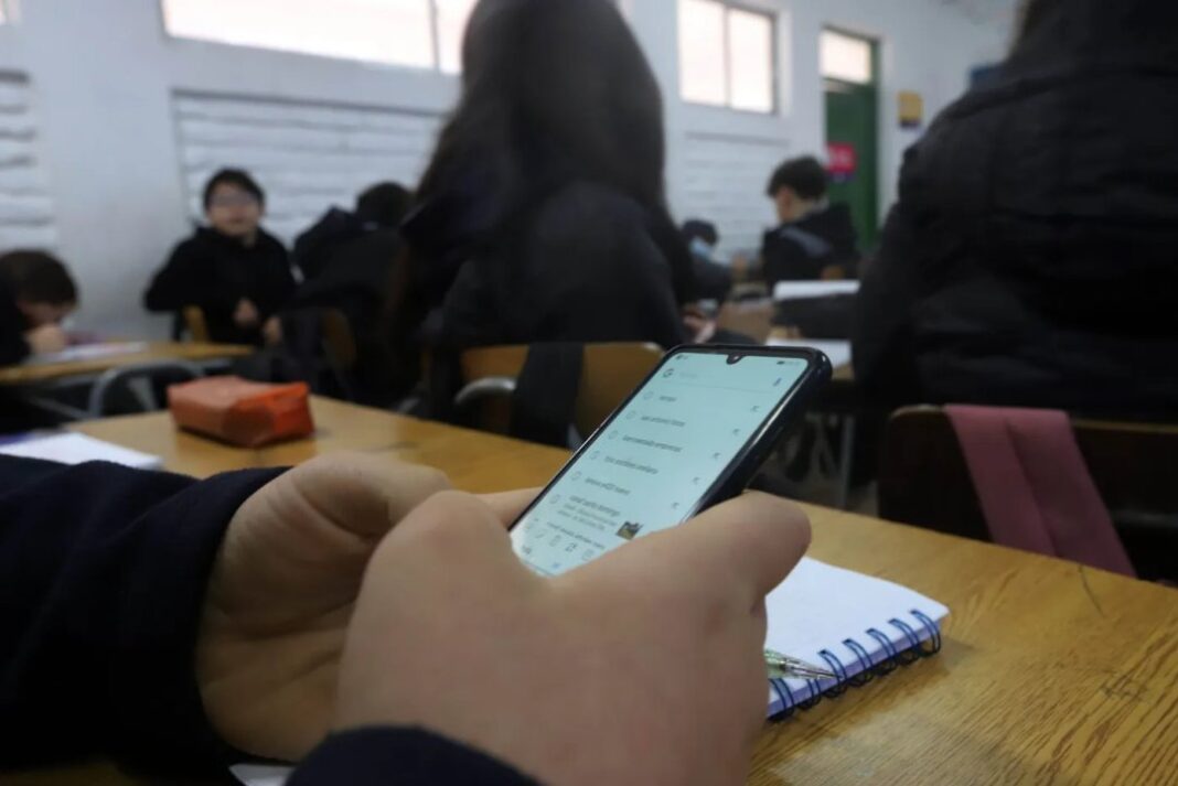 Imagen de un aula con estudiantes y cartel de prohibición de celulares