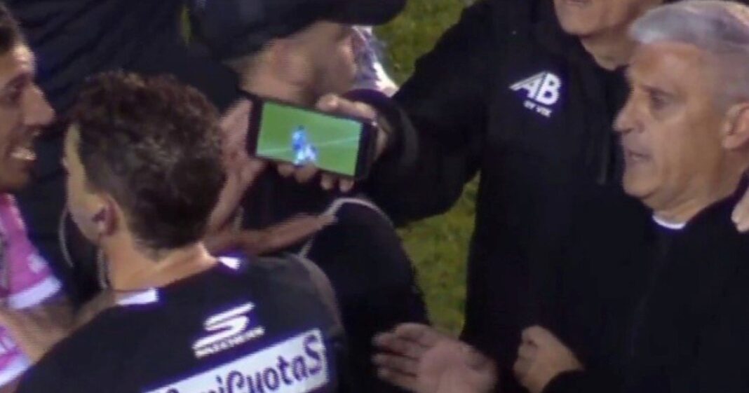 Árbitro Nicolás Lamolina observa un celular que le muestran jugadores de All Boys durante el partido ante Godoy Cruz